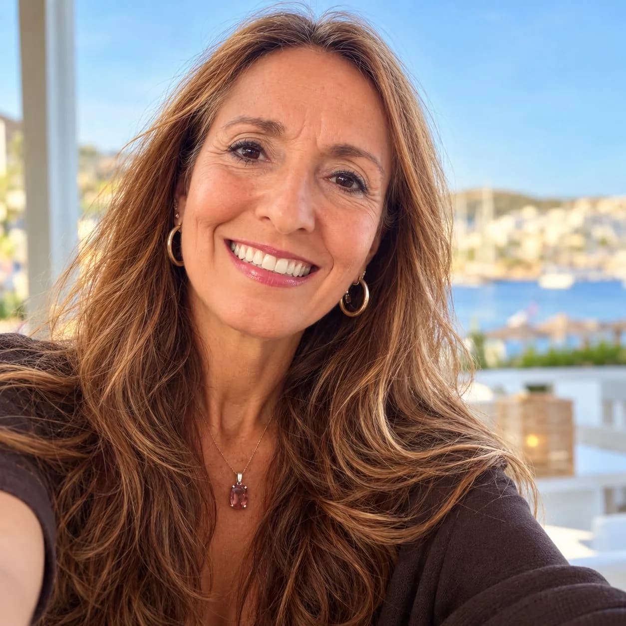 Andrea smiling on a terrace, the sea and a white village behind her.