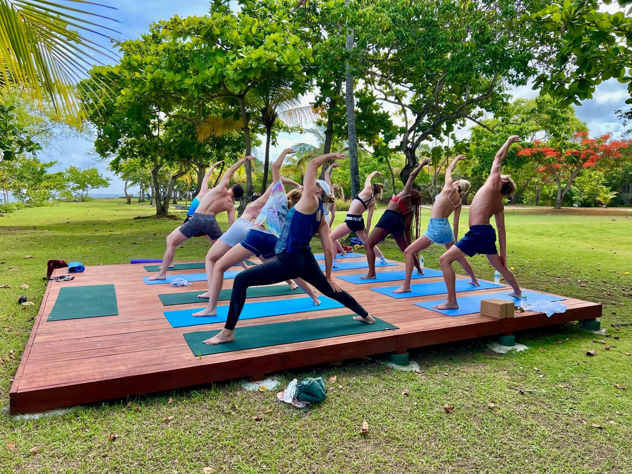 Group class on a wooden platform on the lawn, among trees.
